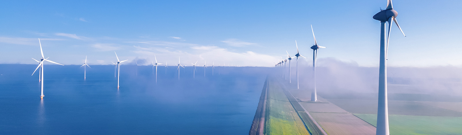 A view of offshore and onshore wind turbines, against a blue sky