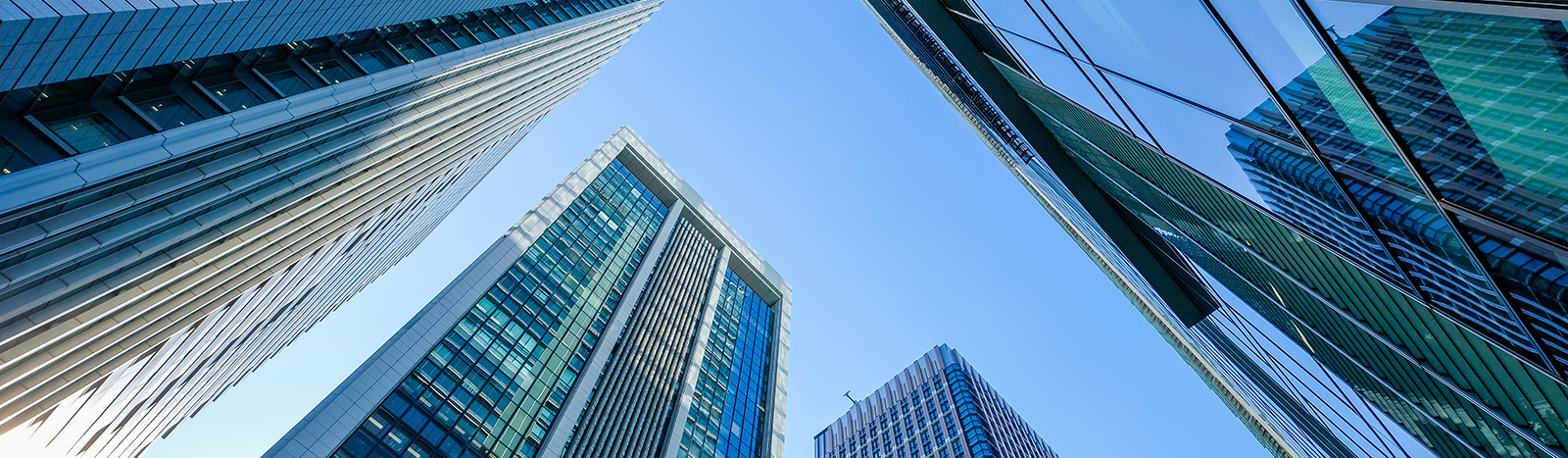 A view of looking up at modern high rise buildings, with a blue sky