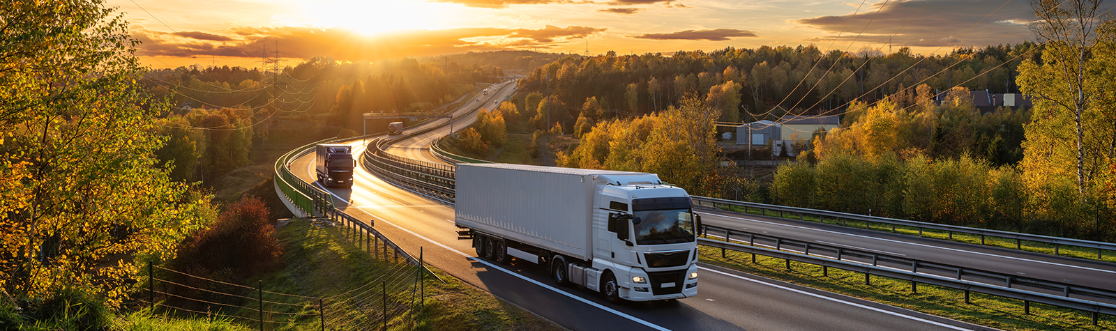 Lorries driving down a highway, with a brilliant sunny sky